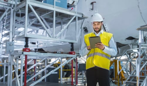 Aircraft Maintenance Mechanics Moving through Hangar. Holding Tablet Computer